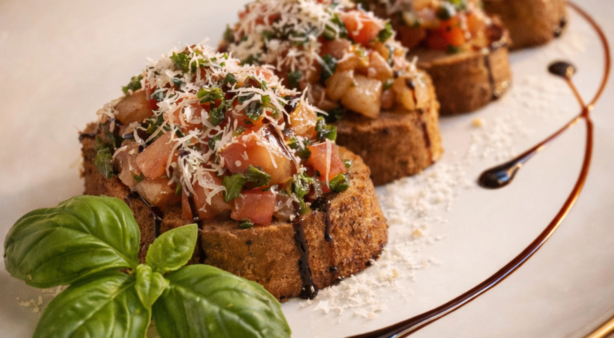 Nahaufnahme von Bruscetta mit frischen Tomaten, frischen Basilikum und Parmesan auf einem weißen Teller. Schön angerichtet mit einem Zweig Basilikum sowie Balsamico Essig als Deko.